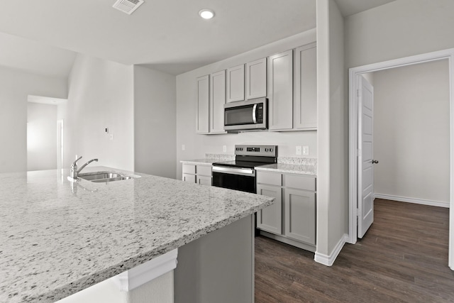 kitchen with a sink, stainless steel appliances, visible vents, dark wood-style flooring, and light stone countertops