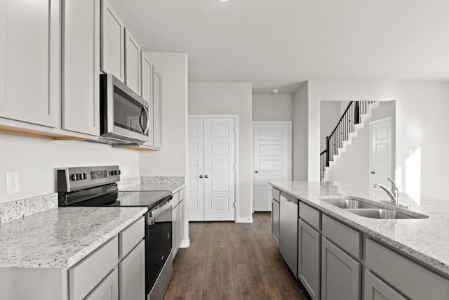 kitchen featuring light stone countertops, gray cabinetry, dark wood finished floors, a sink, and stainless steel appliances