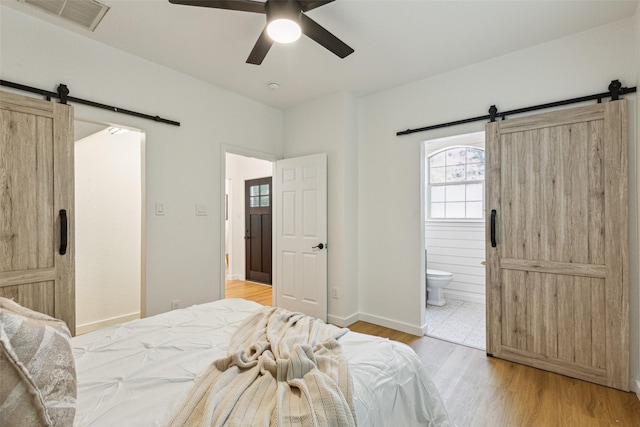627 N Hampton Rd, Dallas, TX 75208 - bedroom with a barn door, light wood-type flooring, connected bathroom, and baseboards