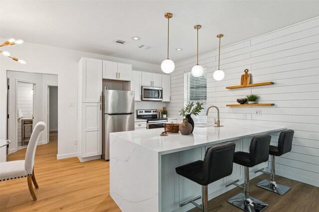 627 N Hampton Rd, Dallas, TX 75208 - kitchen with stainless steel appliances, a sink, light wood finished floors, a kitchen breakfast bar, and white cabinetry