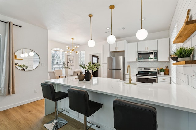 627 N Hampton Rd, Dallas, TX 75208 - kitchen with appliances with stainless steel finishes, a peninsula, decorative backsplash, a chandelier, and light wood-style flooring