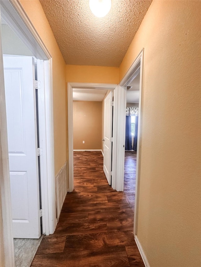 hallway with dark wood-style flooring, visible vents, baseboards, and a textured ceiling
