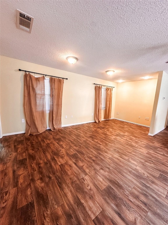 empty room featuring a textured ceiling, wood finished floors, baseboards, and visible vents