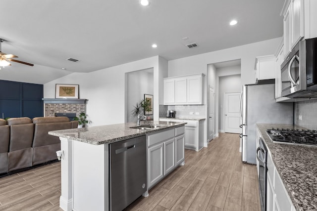 kitchen with open floor plan, appliances with stainless steel finishes, a ceiling fan, light wood finished floors, and backsplash