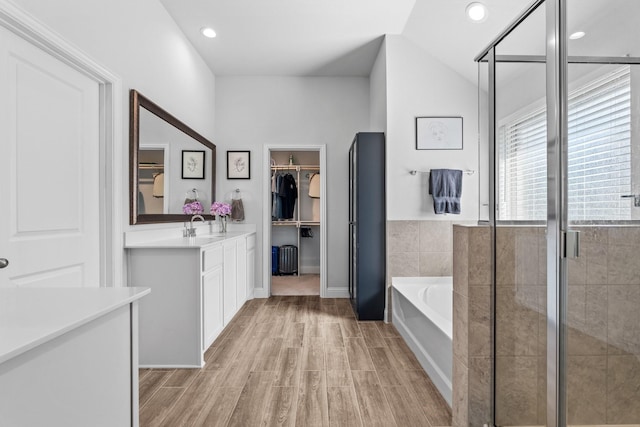 full bathroom featuring a garden tub, vanity, recessed lighting, wood finished floors, and a walk in closet