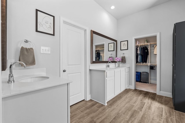 bathroom featuring two vanities, wood finished floors, a sink, and a walk in closet