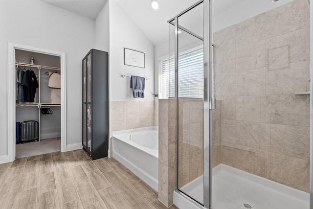 full bathroom featuring a walk in closet, a bath, a stall shower, and lofted ceiling