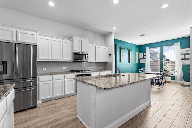 kitchen with stainless steel appliances, white cabinetry, a sink, and stone counters