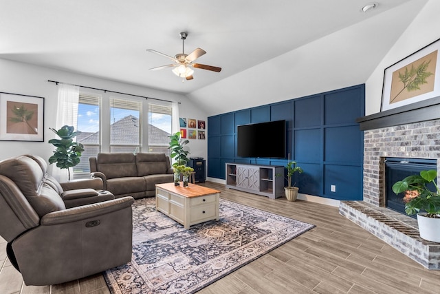 living room with light wood-type flooring, a ceiling fan, vaulted ceiling, and a fireplace