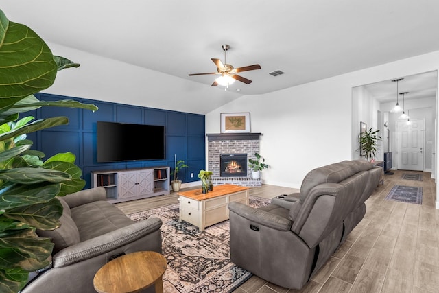 living area with visible vents, a brick fireplace, a ceiling fan, wood finished floors, and lofted ceiling