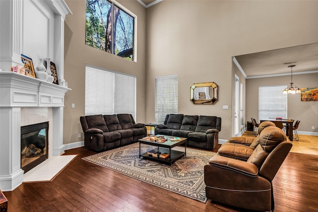 living area with crown molding, a fireplace with flush hearth, a towering ceiling, a notable chandelier, and hardwood / wood-style flooring