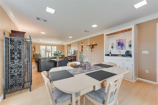 dining space featuring light wood-style floors, ornamental molding, and wet bar
