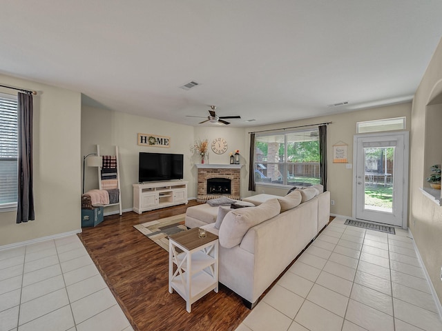 living area with light tile patterned floors, ceiling fan, a fireplace, visible vents, and baseboards