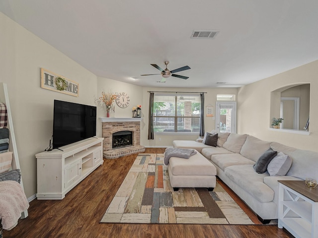 living area featuring ceiling fan, a fireplace, visible vents, dark wood-style flooring, and baseboards