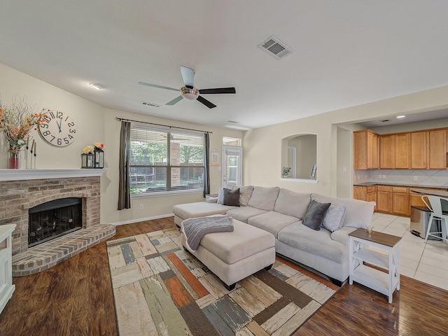 living room featuring visible vents, light wood-style flooring, ceiling fan, and a brick fireplace