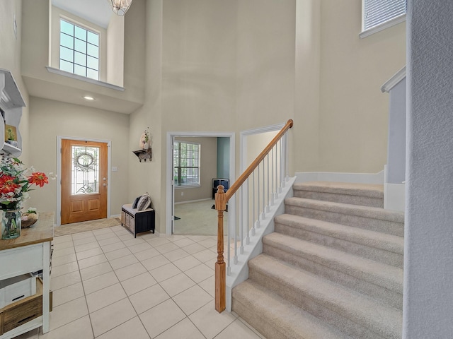 entrance foyer featuring light tile patterned floors, baseboards, a towering ceiling, and stairs
