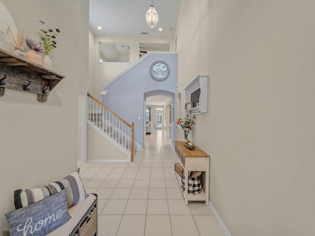 foyer entrance with arched walkways, a towering ceiling, light tile patterned flooring, stairs, and baseboards