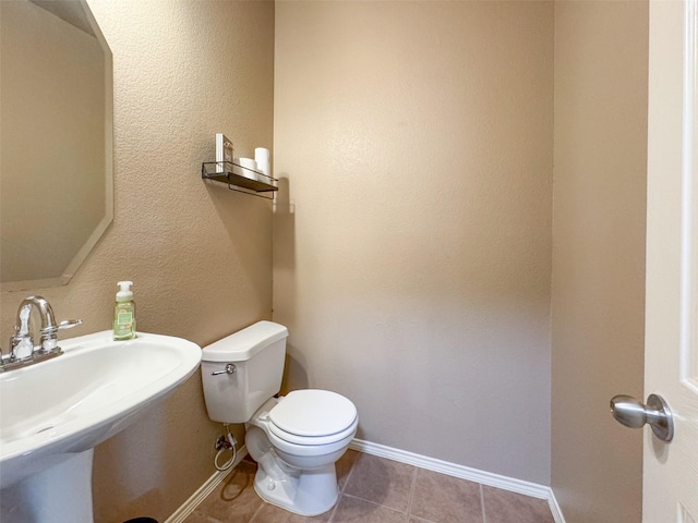 half bath featuring toilet, tile patterned floors, a sink, and baseboards