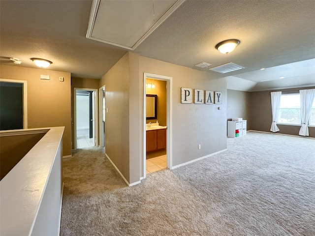 interior space with visible vents, attic access, light colored carpet, and a textured ceiling