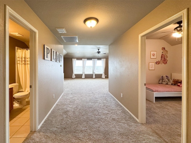 hallway featuring carpet floors, a textured wall, visible vents, and a textured ceiling