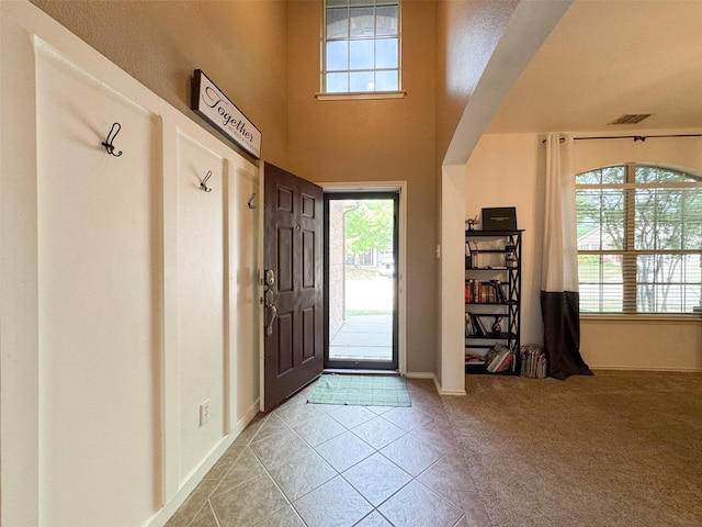 carpeted foyer with tile patterned floors, a high ceiling, baseboards, and visible vents