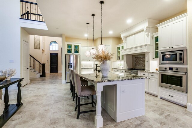 kitchen with tasteful backsplash, an island with sink, glass insert cabinets, appliances with stainless steel finishes, and white cabinetry