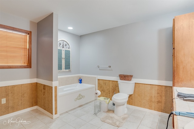 full bathroom with tile patterned flooring, a wainscoted wall, a garden tub, and toilet