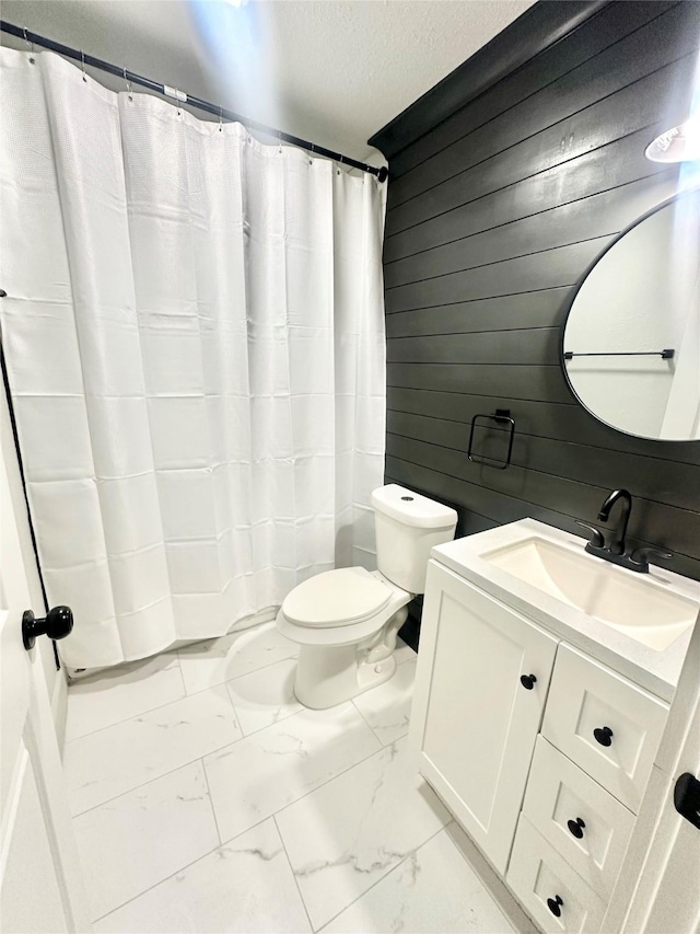 full bath with a textured ceiling, vanity, toilet, wood walls, and marble finish floor