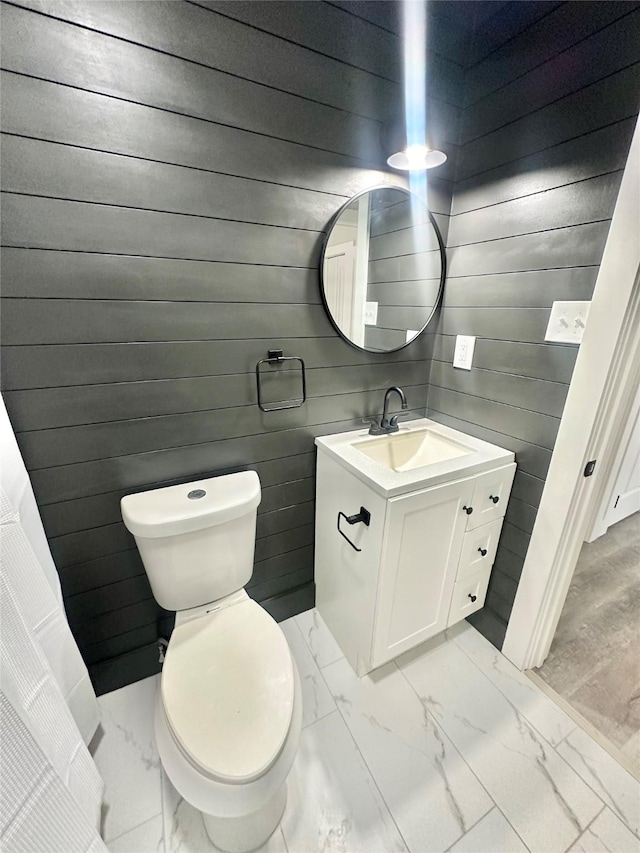 bathroom with toilet, wood walls, marble finish floor, and vanity
