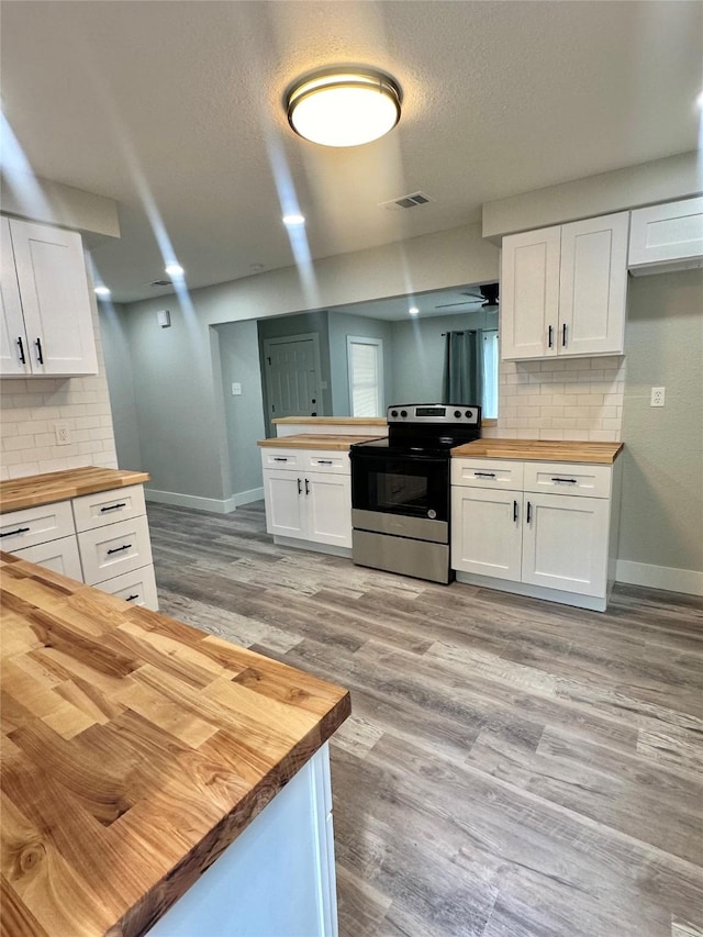 kitchen featuring stainless steel range with electric stovetop, white cabinetry, backsplash, and wooden counters