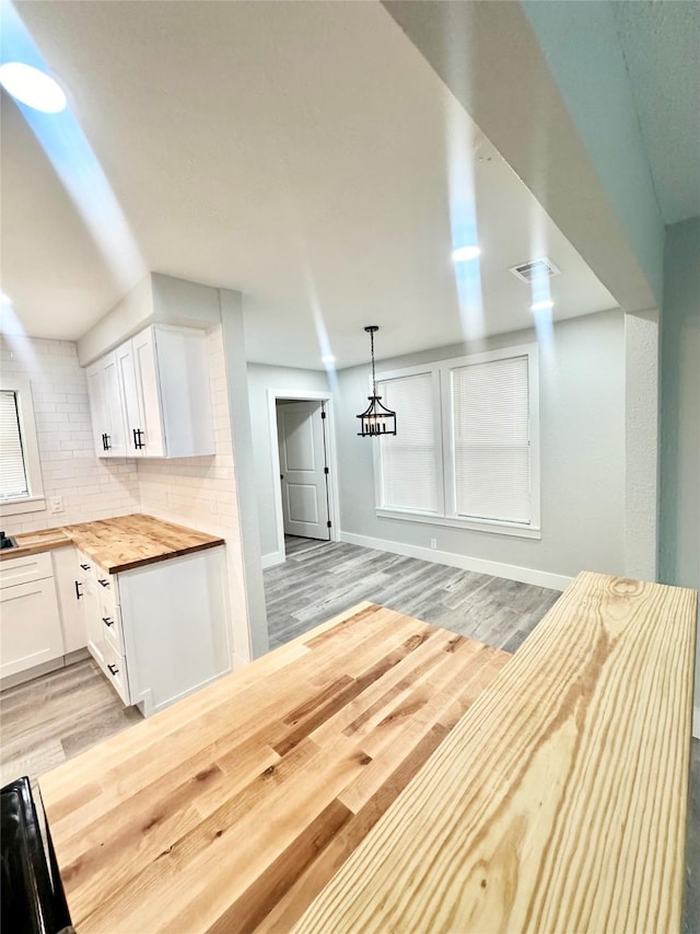 kitchen with tasteful backsplash, butcher block countertops, baseboards, white cabinetry, and light wood-style floors
