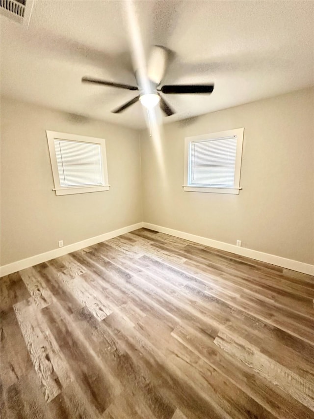empty room with baseboards, a textured ceiling, visible vents, ceiling fan, and wood finished floors