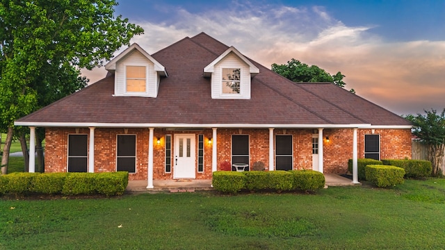 view of front of house featuring a porch, a shingled roof, a yard, and brick siding