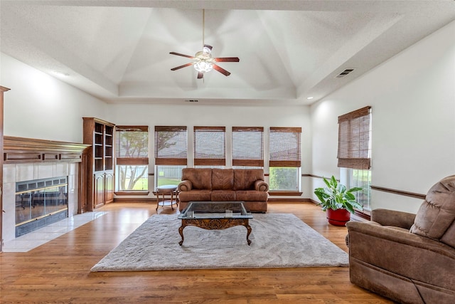 living room featuring a ceiling fan, visible vents, a tile fireplace, a tray ceiling, and recessed lighting