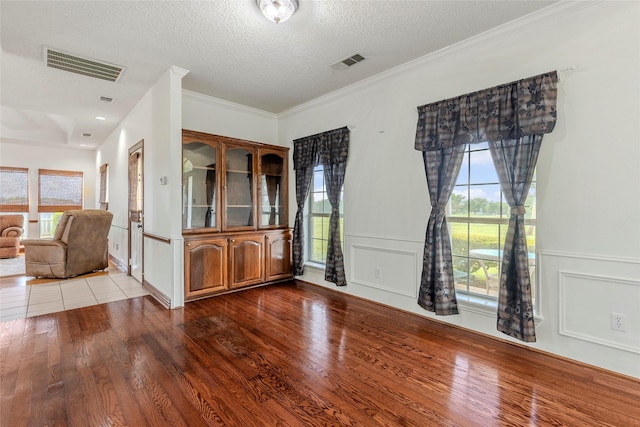 interior space featuring visible vents, ornamental molding, a textured ceiling, and wood finished floors
