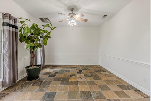 empty room with visible vents, a ceiling fan, stone finish flooring, and a textured ceiling