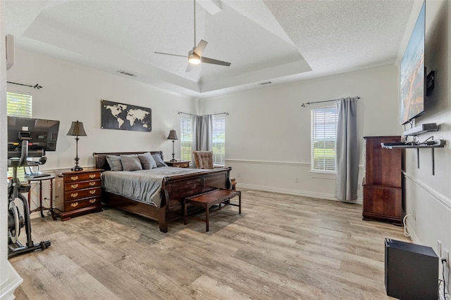 bedroom with visible vents, light wood-style flooring, and a raised ceiling