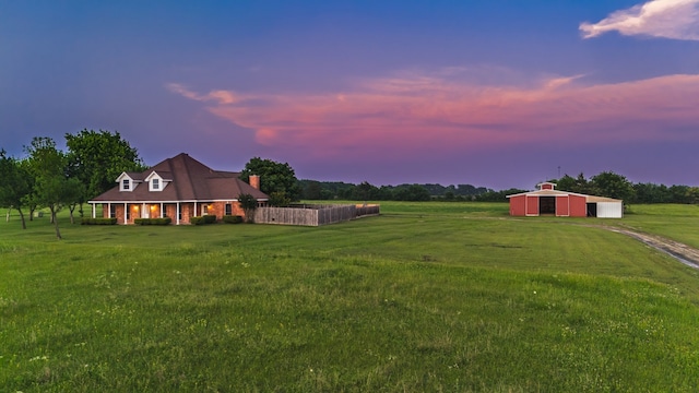 yard at dusk featuring driveway, an outbuilding, a detached garage, a pole building, and a rural view