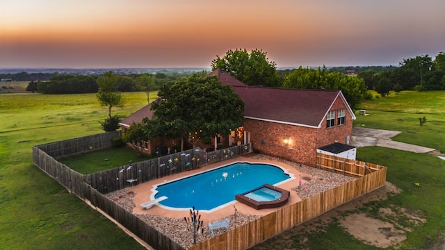 pool at dusk with a diving board, a pool with connected hot tub, a fenced backyard, a patio area, and a lawn
