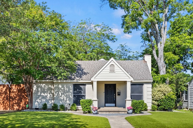view of front of property with a front lawn, a shingled roof, a chimney, brick siding, and a porch