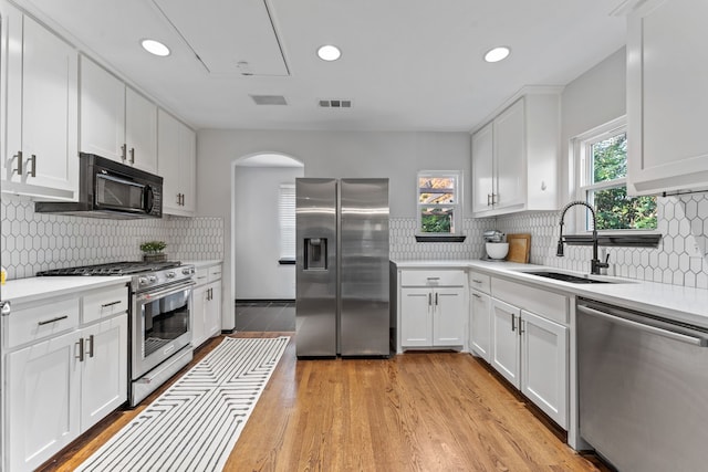kitchen featuring appliances with stainless steel finishes, a sink, light wood finished floors, light countertops, and white cabinetry