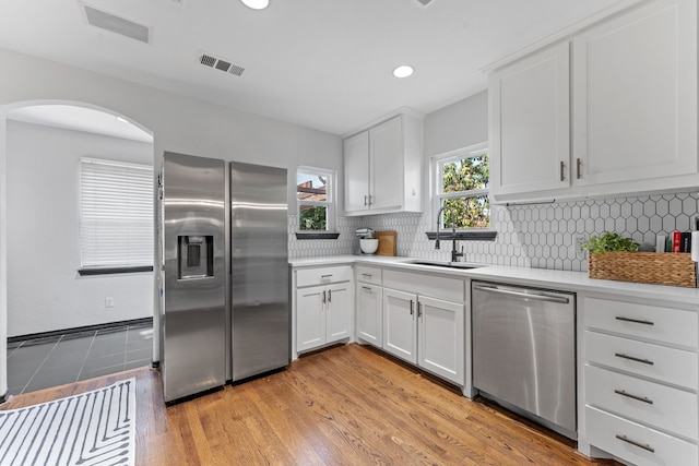 kitchen featuring stainless steel appliances, a sink, light countertops, arched walkways, and white cabinetry