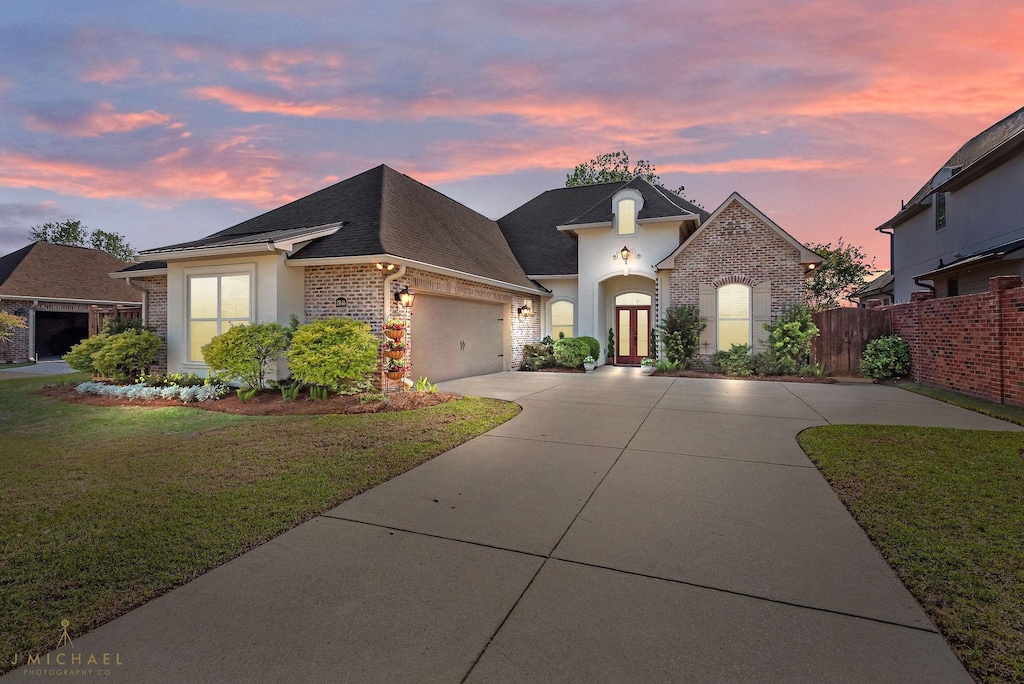 2848 Caribbean Cv, Shreveport, LA 71105 - french country inspired facade featuring a shingled roof, a yard, an attached garage, concrete driveway, and brick siding
