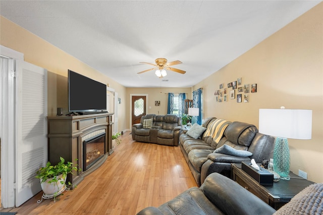 living room with a ceiling fan, light wood finished floors, and a glass covered fireplace