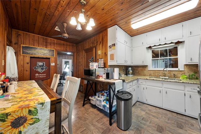 kitchen with a sink, wood walls, stainless steel microwave, wooden ceiling, and decorative backsplash