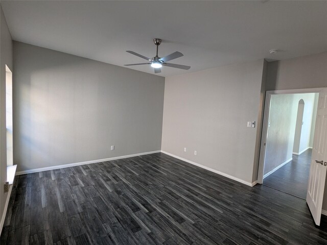 spare room featuring dark wood-style floors, arched walkways, ceiling fan, and baseboards