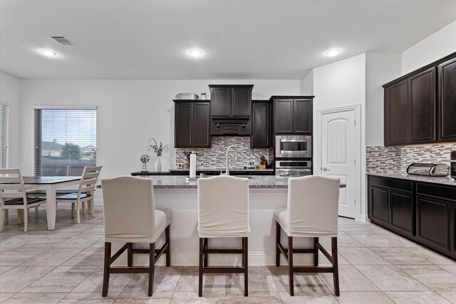 525 Northwood Dr, Oak Point, TX 75068 - kitchen with appliances with stainless steel finishes, a breakfast bar area, tasteful backsplash, light stone countertops, and recessed lighting