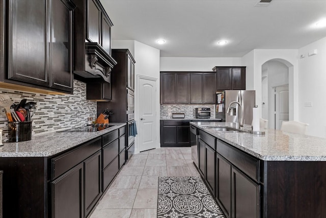 525 Northwood Dr, Oak Point, TX 75068 - kitchen with a sink, appliances with stainless steel finishes, a kitchen island with sink, decorative backsplash, and arched walkways