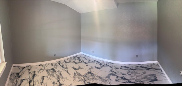 spare room featuring vaulted ceiling, marble finish floor, and baseboards