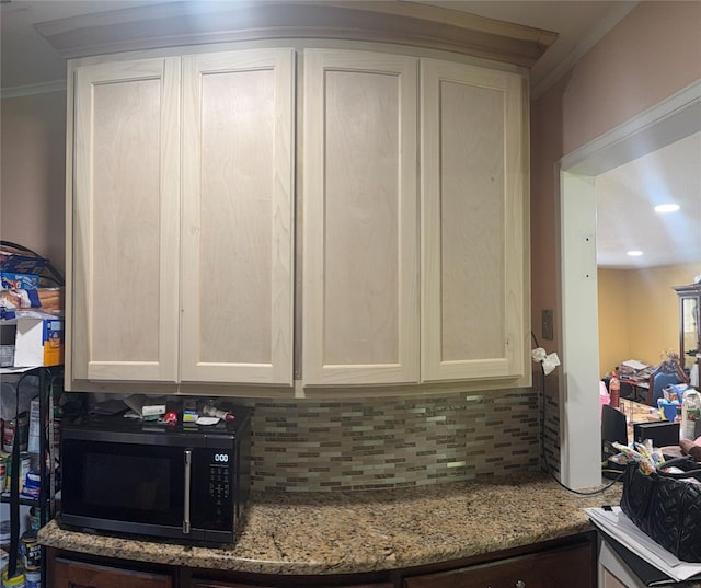 interior details with ornamental molding, black microwave, white cabinetry, backsplash, and light stone countertops